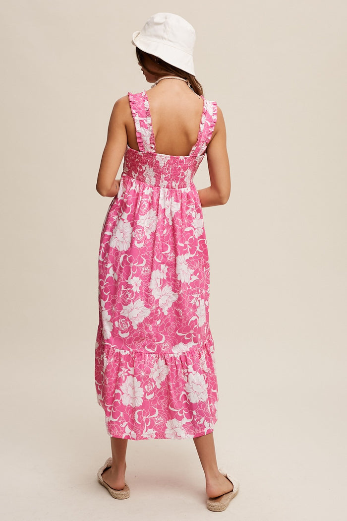 woman wearing a pink floral maxi dress with a smocked back and tiered hem, styled with a white bucket hat