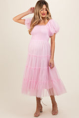 woman wearing a pink maternity dress with puff sleeves and a tiered tulle skirt, gently holding her hair