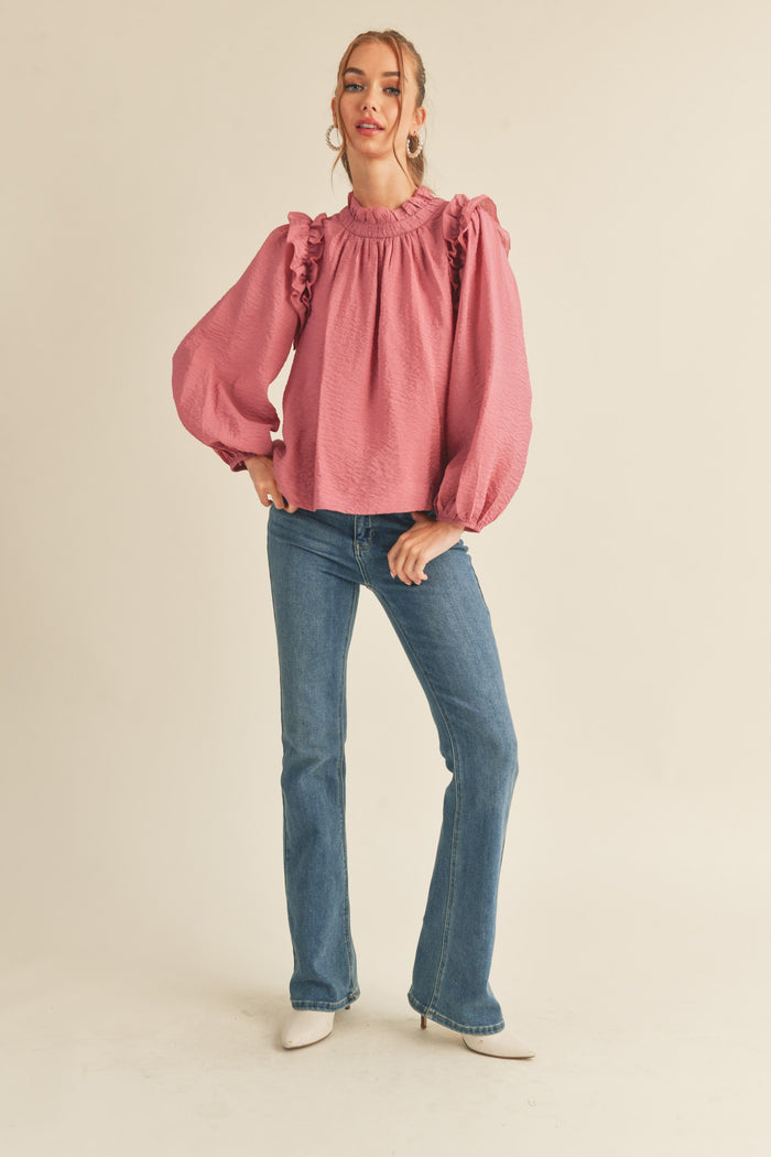 woman wearing a pink ruffled blouse with puff sleeves and blue flared jeans