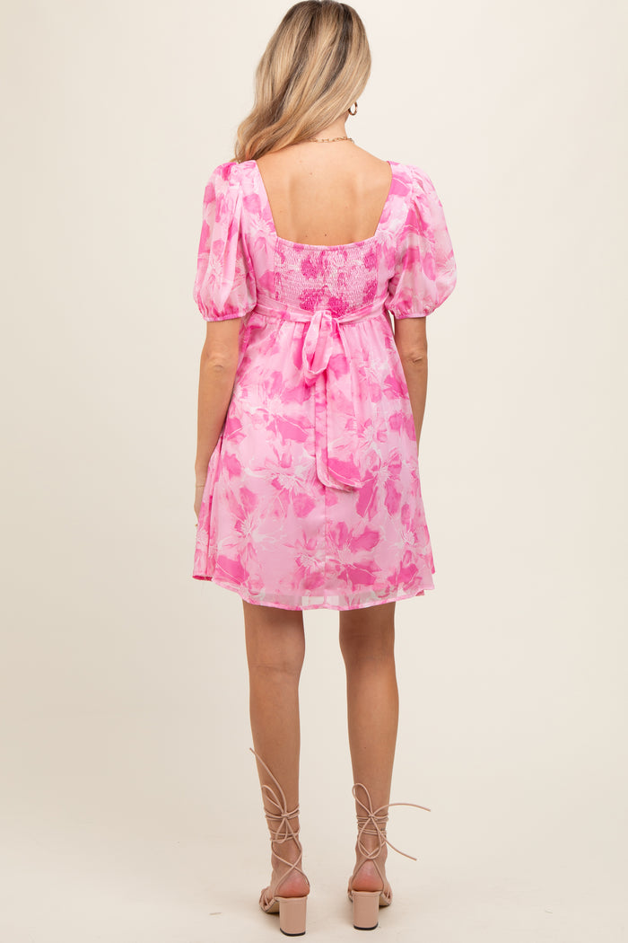 woman wearing a pink floral maternity dress with puff sleeves and a tie-back detail, showing her baby bump