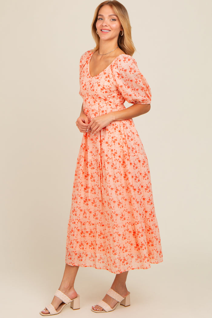 woman wearing a light peach floral midi dress with puff sleeves and a square neckline, posing against a neutral background