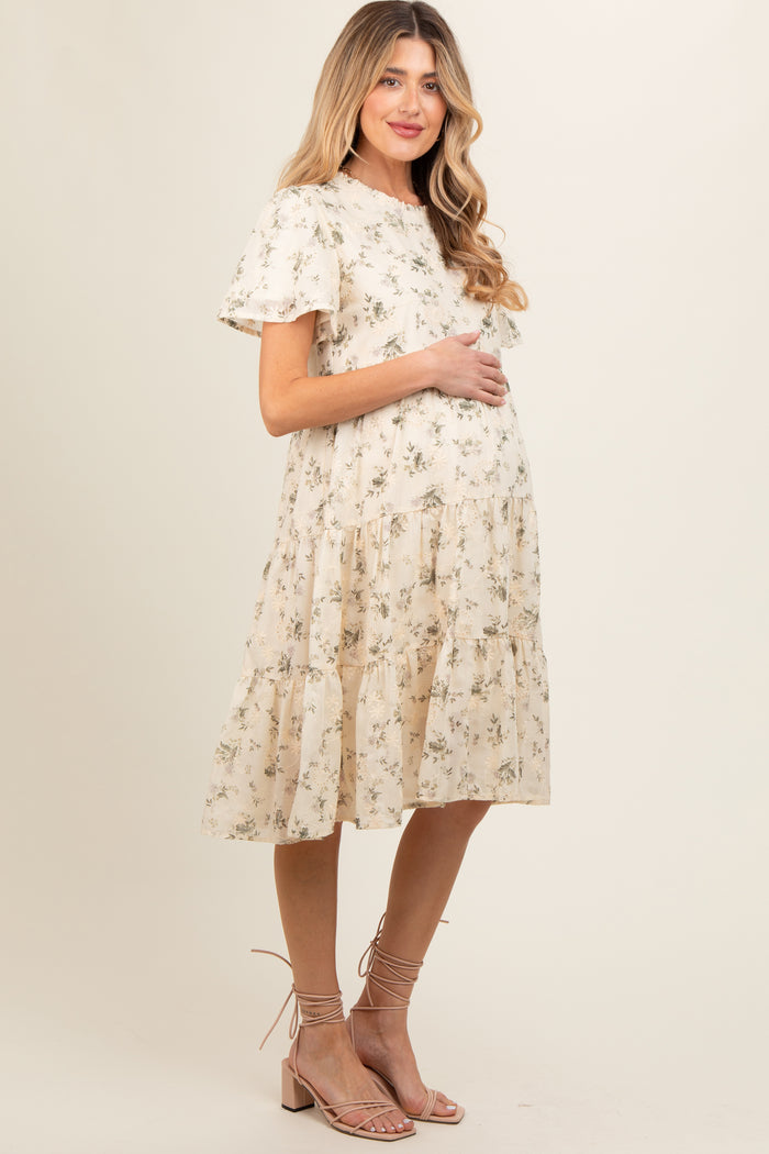 woman wearing a cream floral print maternity dress with short sleeves and a tiered skirt, holding her baby bump