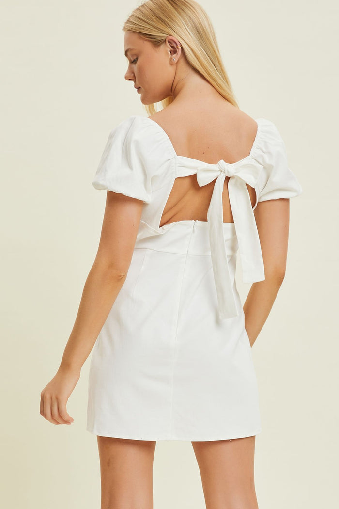 woman wearing a white short dress with puff sleeves and a back tie detail