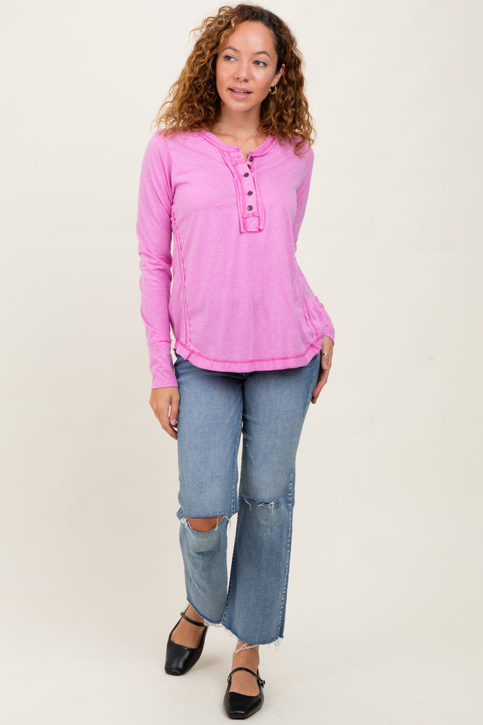 woman wearing a pink long sleeve henley top with button details and distressed light blue jeans