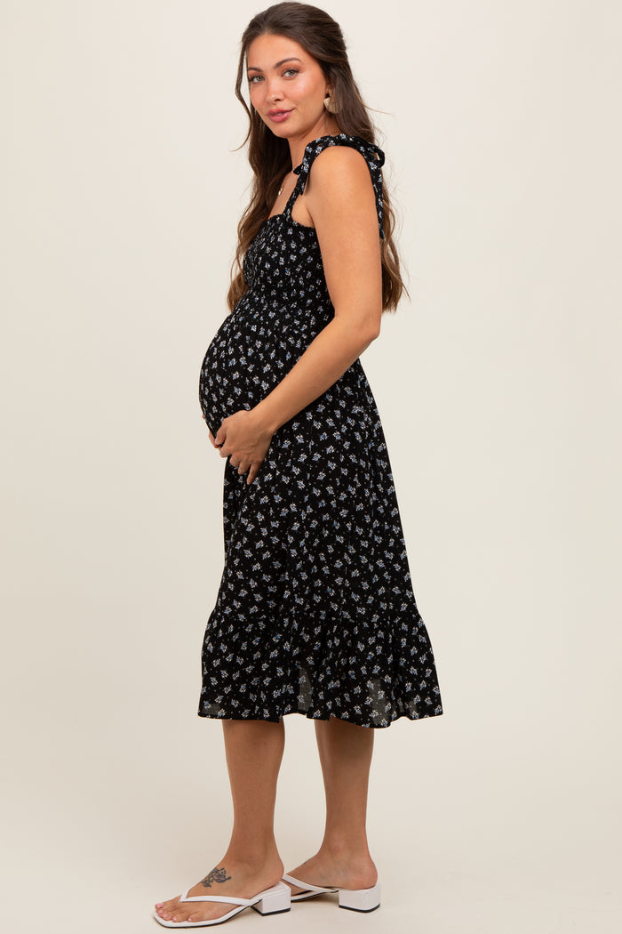 woman wearing a black floral maternity dress with tie straps, highlighting her baby bump while standing sideways