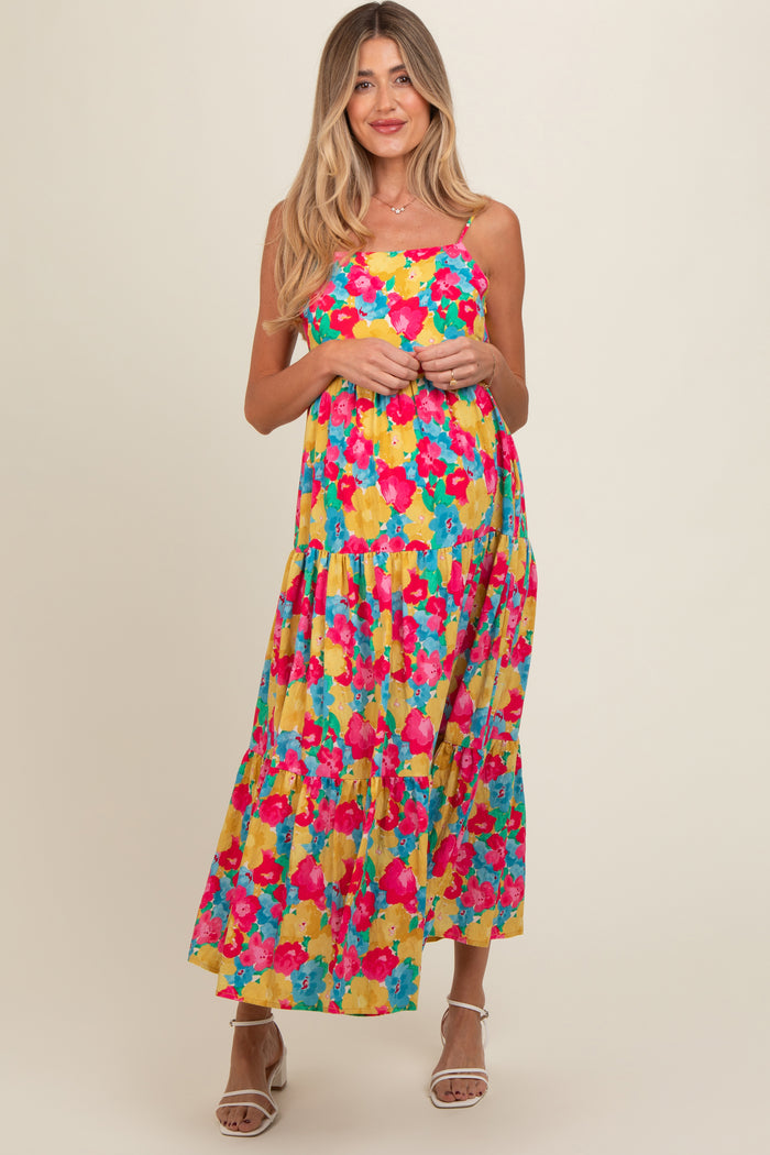 woman wearing a colorful floral maternity maxi dress with a tiered skirt and spaghetti straps, smiling at the camera