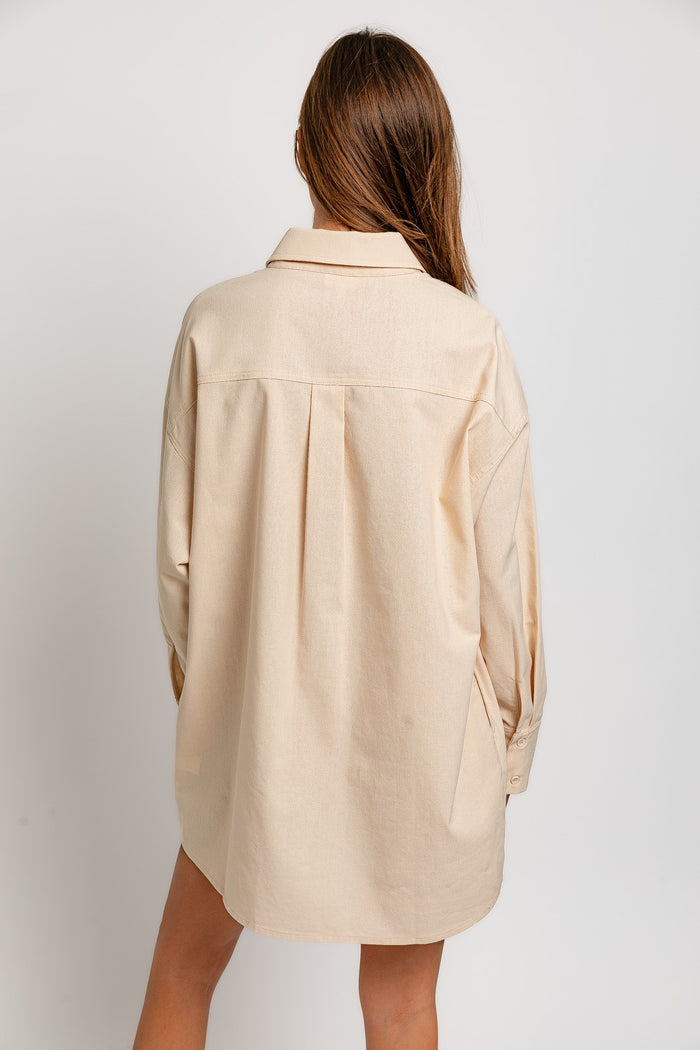 woman wearing a beige oversized button-up shirt with a collar and pleat detail on the back