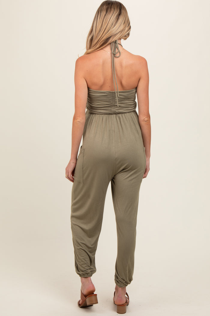 woman wearing an olive green maternity jumpsuit with a halter neck and relaxed fit, showing no baby bump.