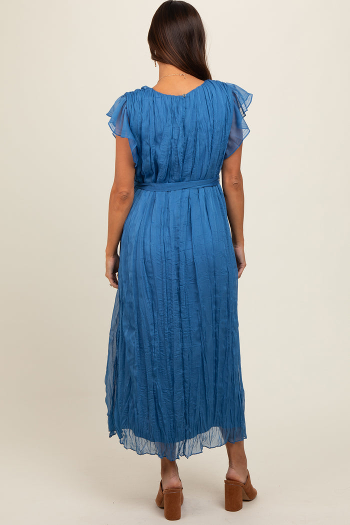 woman wearing a blue flutter sleeve maternity dress with a textured design and a belted waist, showing the back view