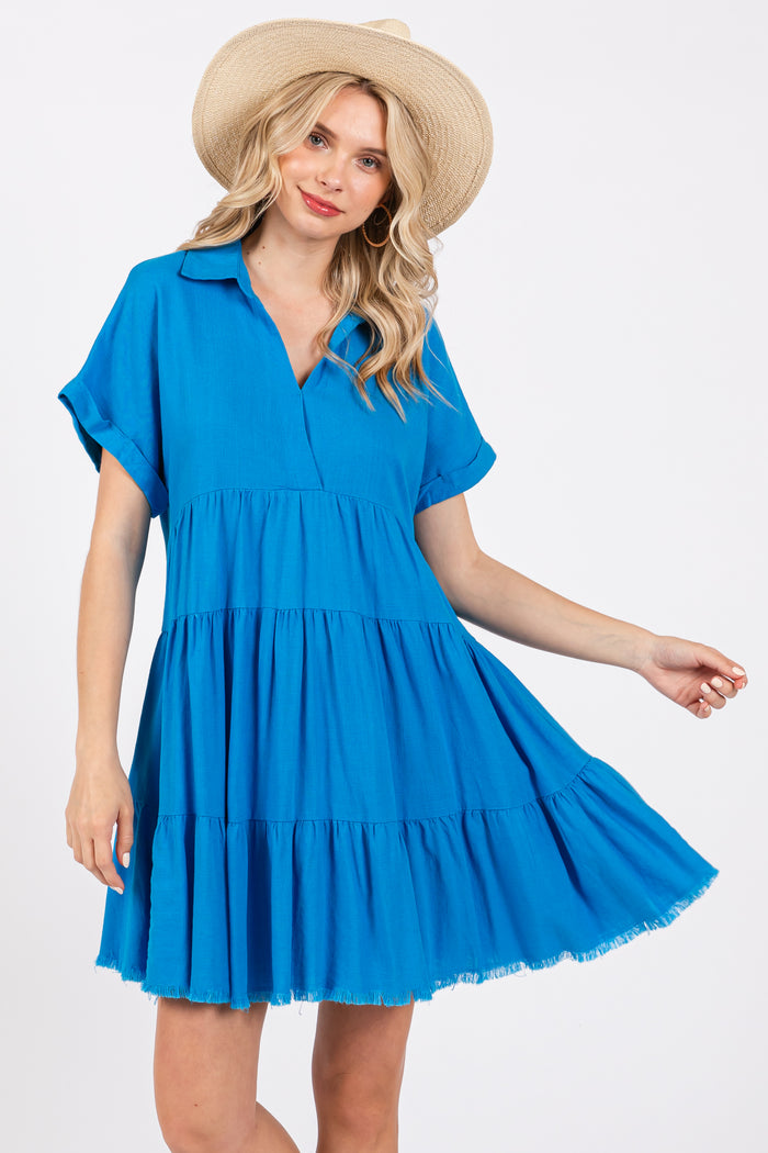 woman wearing a bright blue tiered short dress with a collared neckline and short sleeves, accessorized with a straw hat