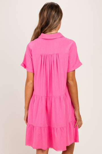 woman wearing a bright pink short sleeve maternity dress with tiered detailing and a collar, showing no visible baby bump