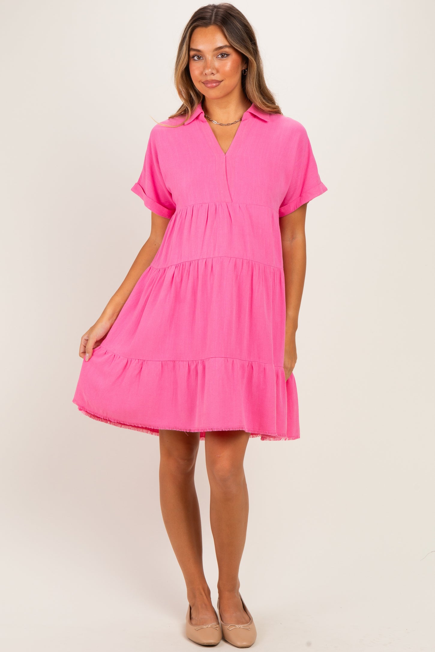 woman wearing a bright pink short sleeve maternity dress with a tiered design and a collar, holding her baby bump