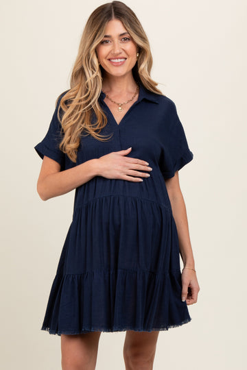 woman wearing a navy blue short sleeve maternity dress with a tiered skirt and a collar, holding her baby bump