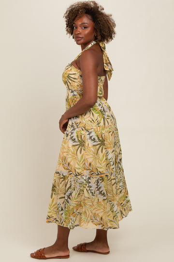 woman wearing a yellow tropical print halter maxi dress with a tie-back detail and flowing skirt