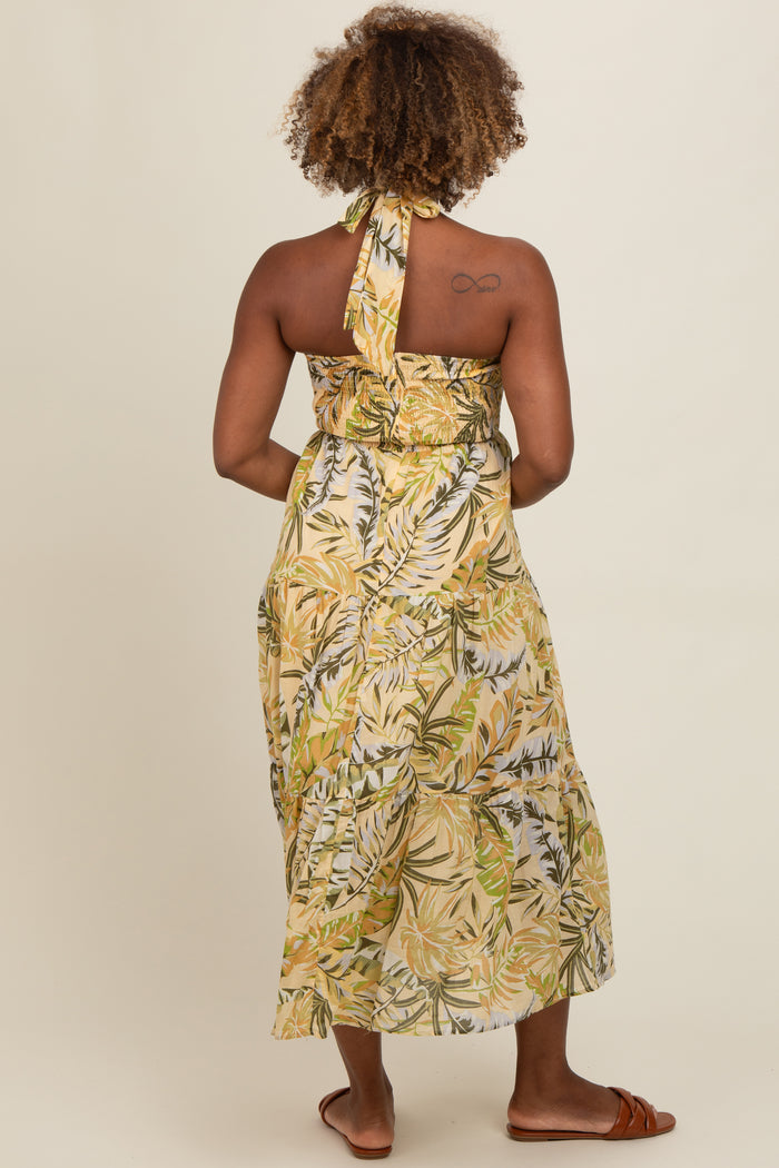 woman wearing a sleeveless yellow tropical print maxi dress with a halter neck and a flowy skirt, shown from the back