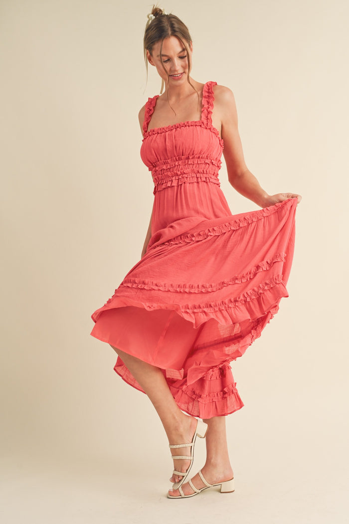 woman wearing a coral ruffled midi dress with a fitted bodice and flared skirt, striking a playful pose