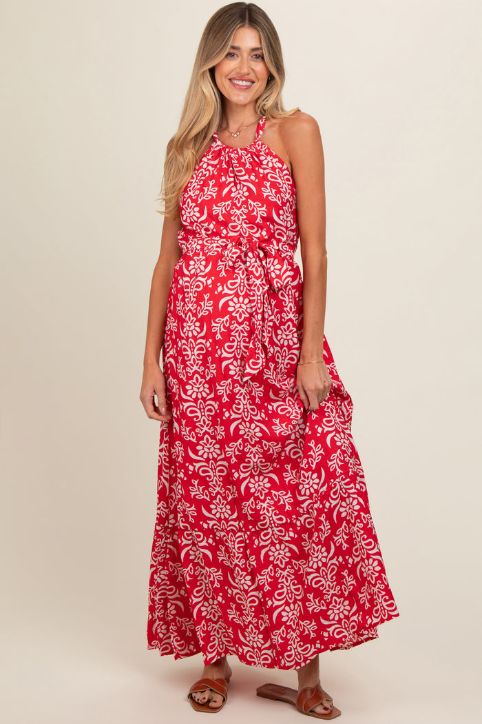 woman wearing a red floral print maternity maxi dress with a halter neckline and tie waist, showing a baby bump