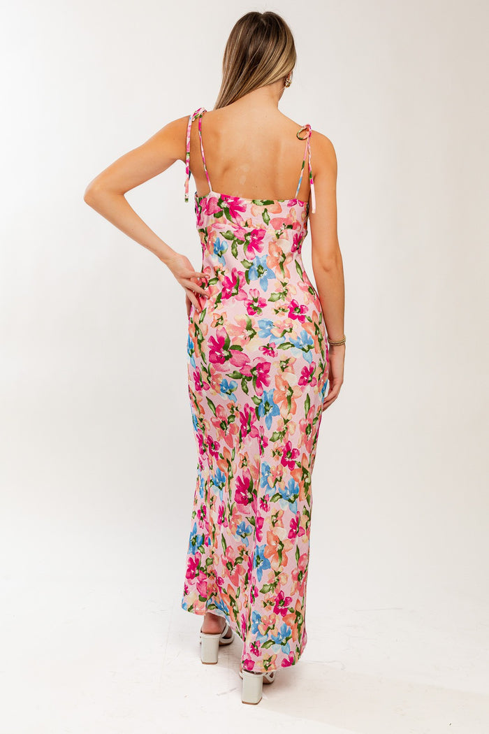 woman wearing a floral maxi dress with a pink background and tie shoulder straps, showing the back view