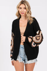 woman wearing a black chunky cardigan with crochet pattern sleeves and styled with a beige top and denim shorts
