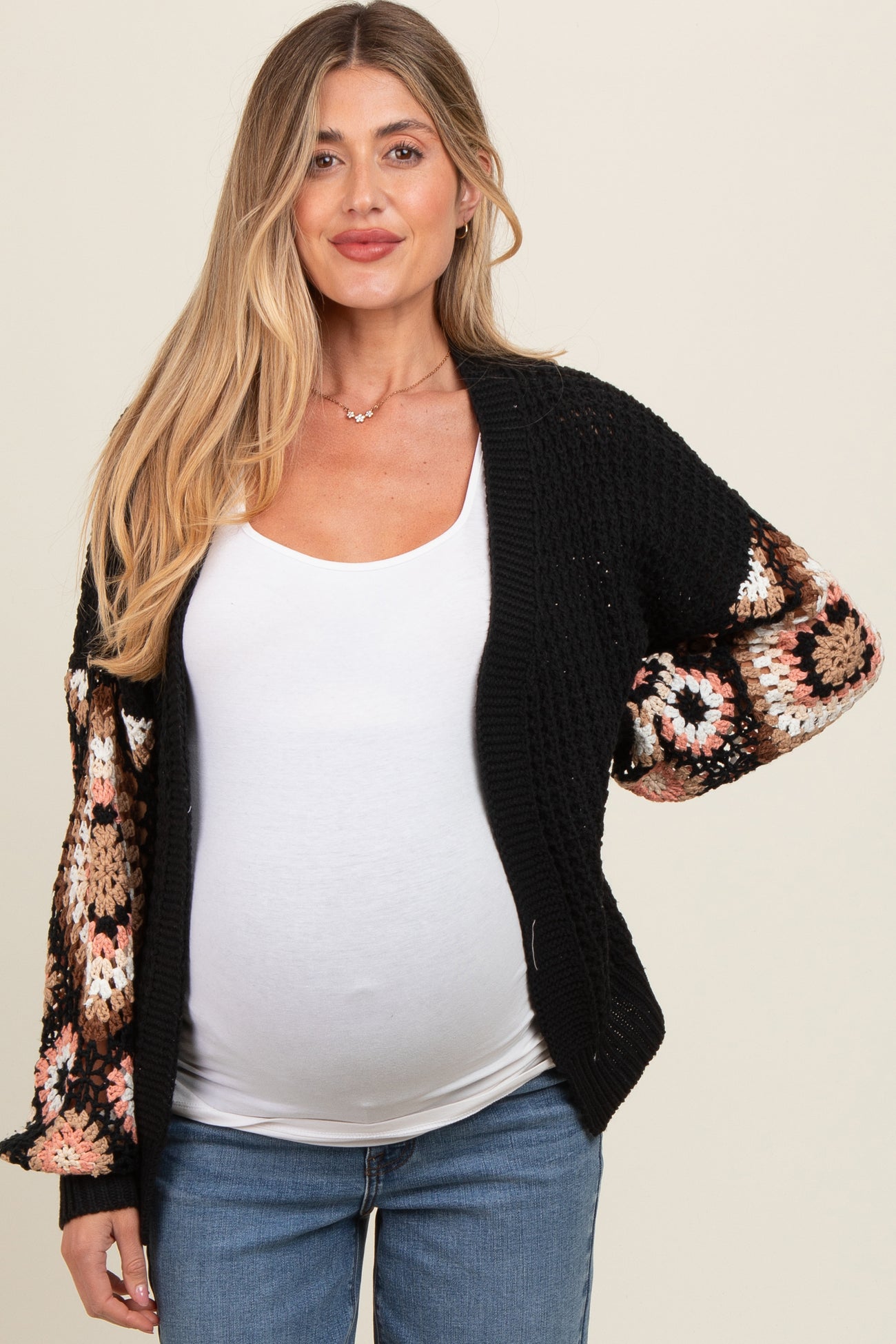 woman wearing a black and multicolor crochet maternity cardigan over a white top and showing her baby bump
