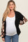 woman wearing a black and multicolor crochet maternity cardigan over a white top and showing her baby bump