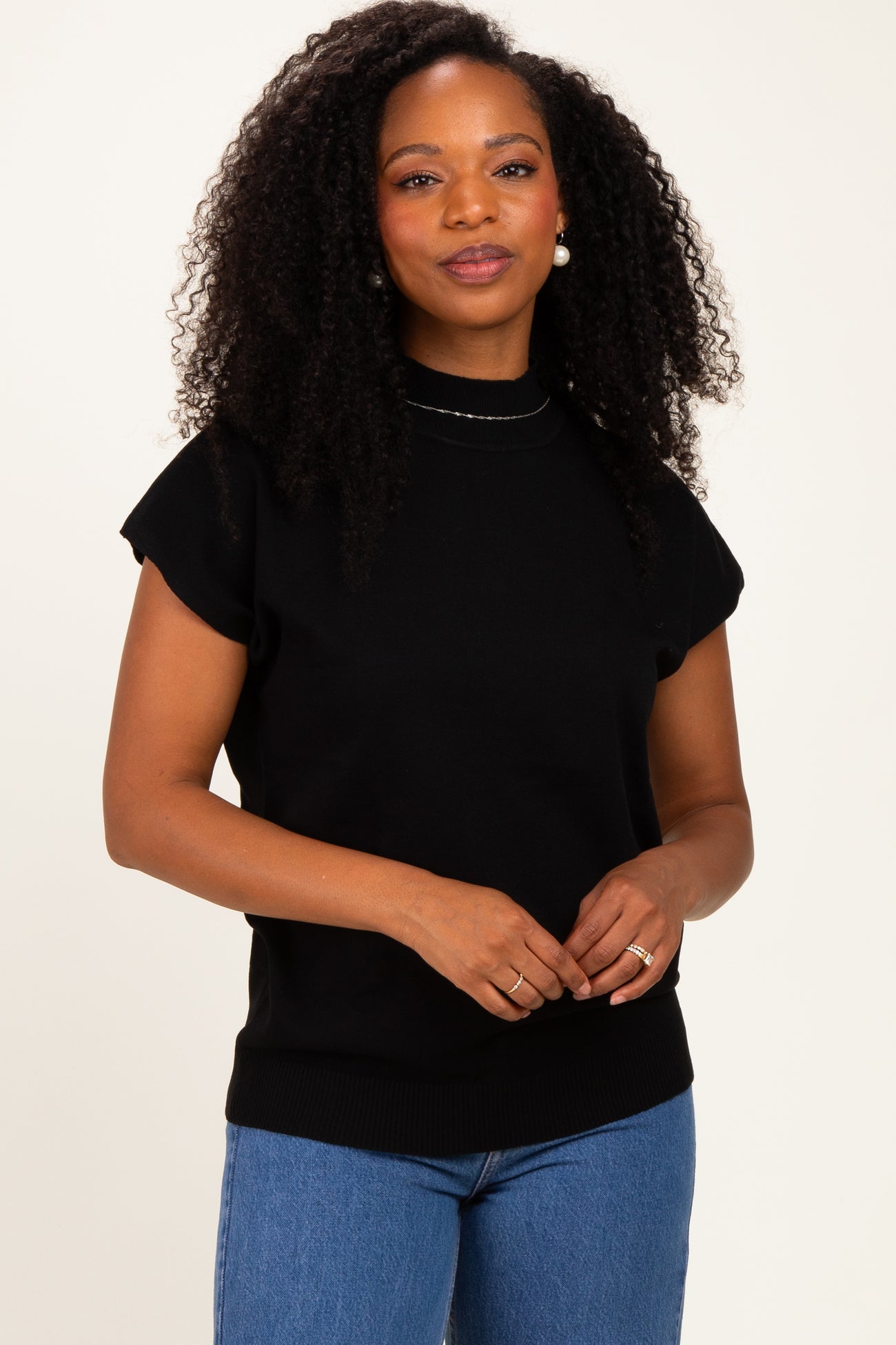 woman wearing a black short sleeve sweater with a mock neck and relaxed fit, paired with blue jeans