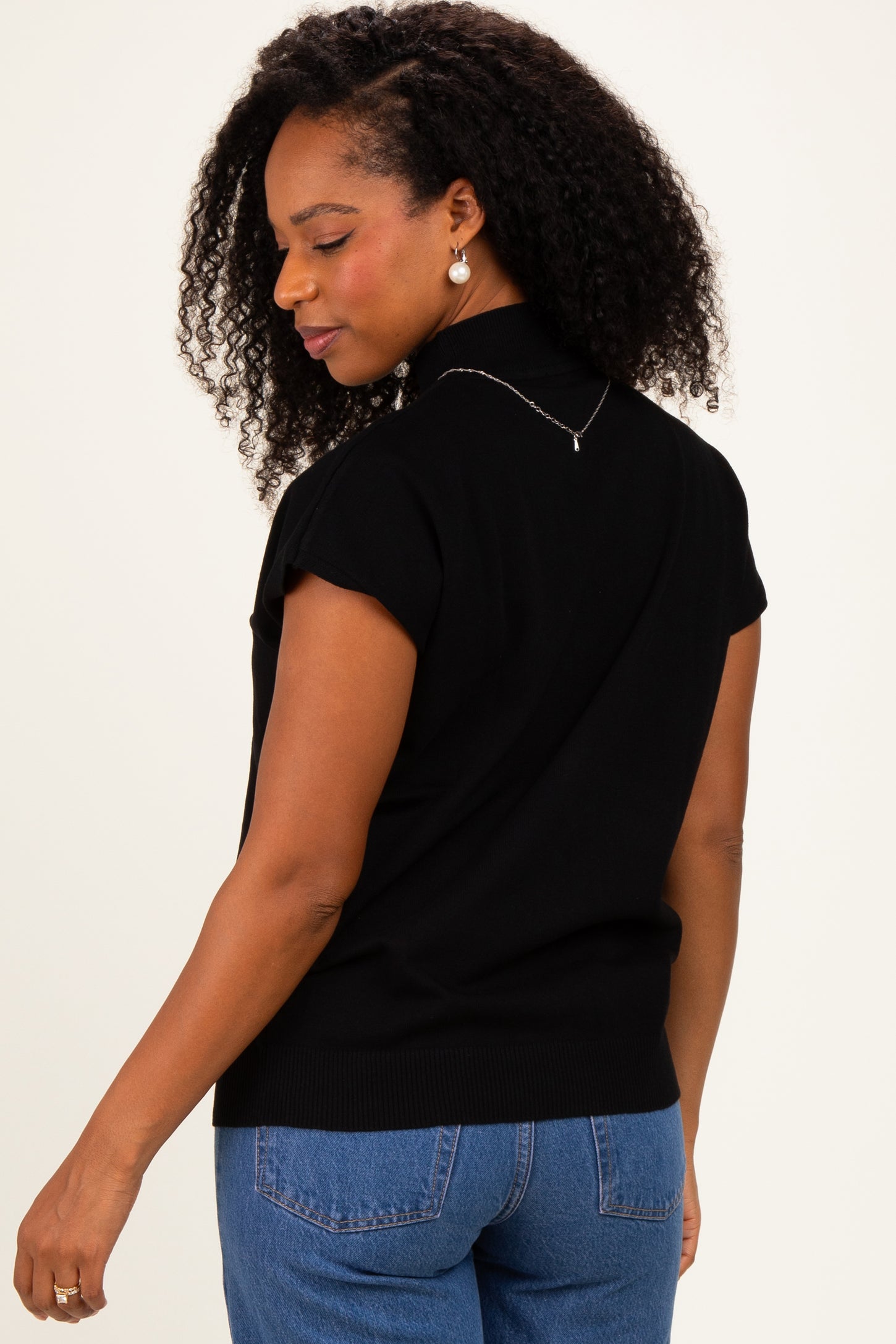 woman wearing a black short sleeve sweater with a ribbed hem and back detail, styled with high-waisted jeans