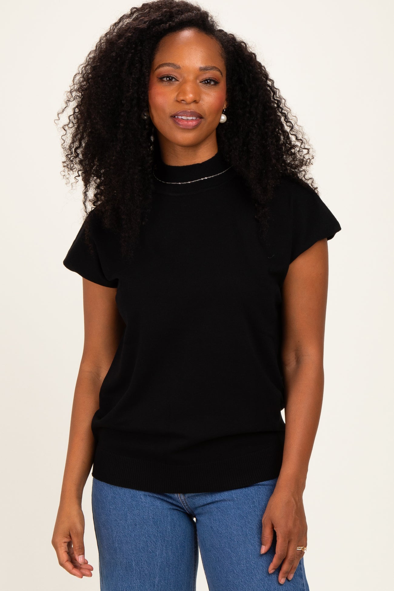 woman wearing a black short sleeve sweater with a high neckline and ribbed hem, standing against a light background