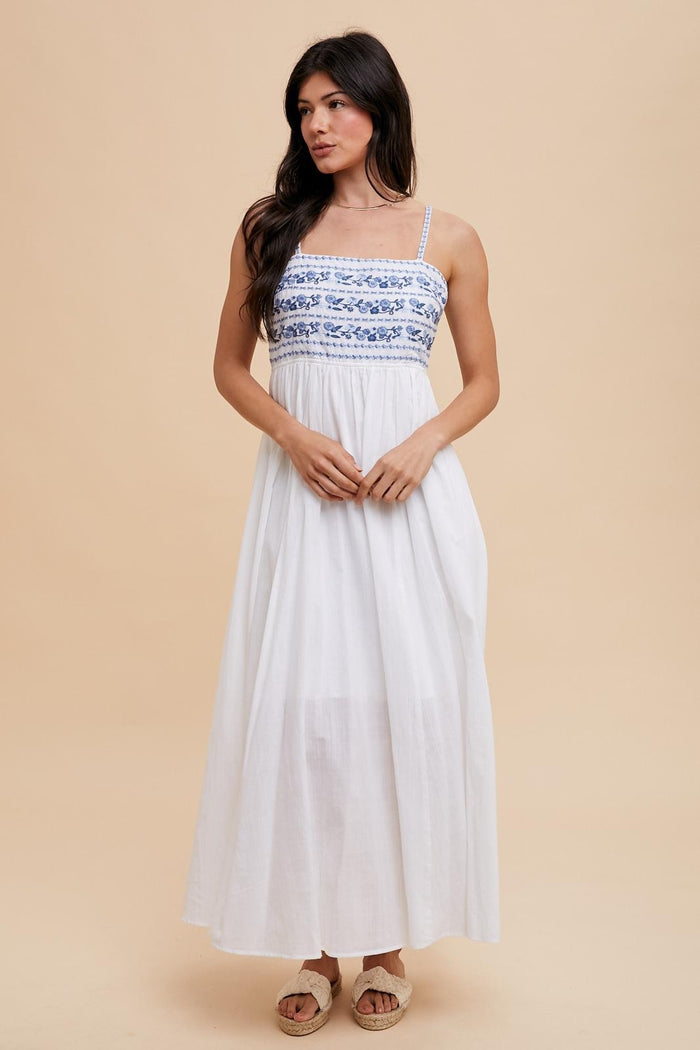 woman wearing a white maxi dress with blue embroidered detailing and thin straps