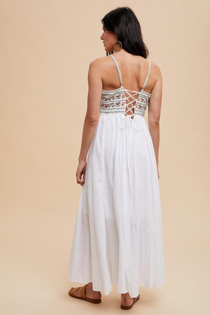 woman wearing a white maxi dress with a floral-embroidered bodice and crisscross back detail
