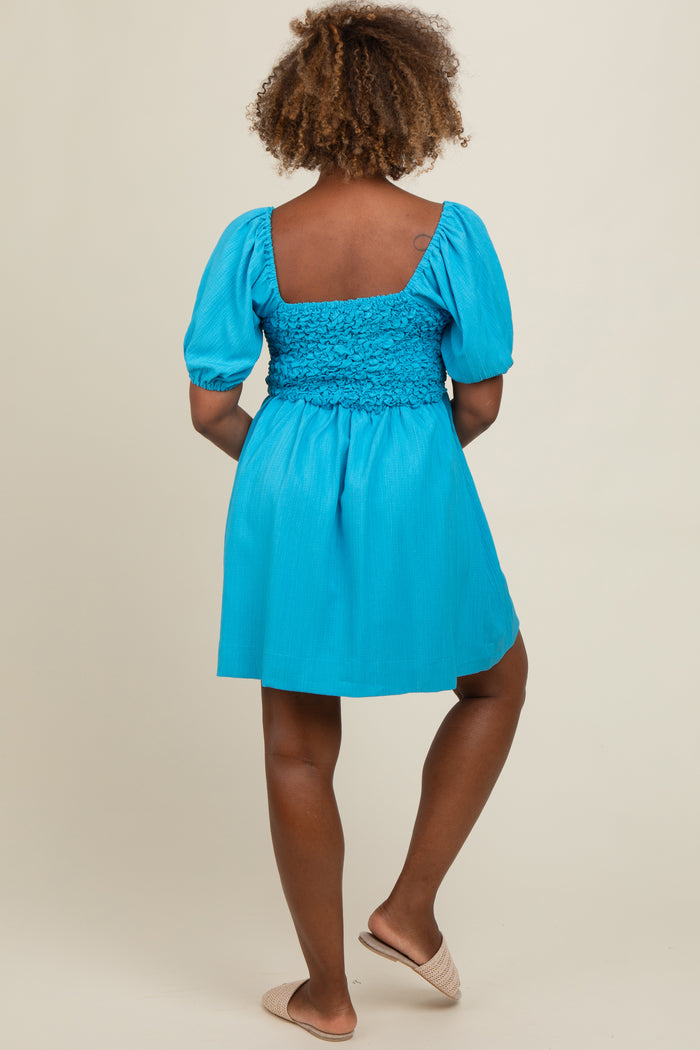 woman wearing a bright blue puff sleeve dress with a smocked bodice and a flared skirt, shown from the back.