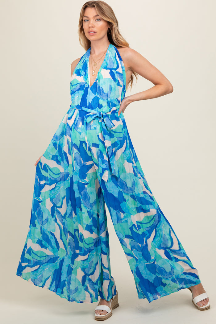 woman wearing a blue and green abstract print maternity jumpsuit with a halter neck and wide legs