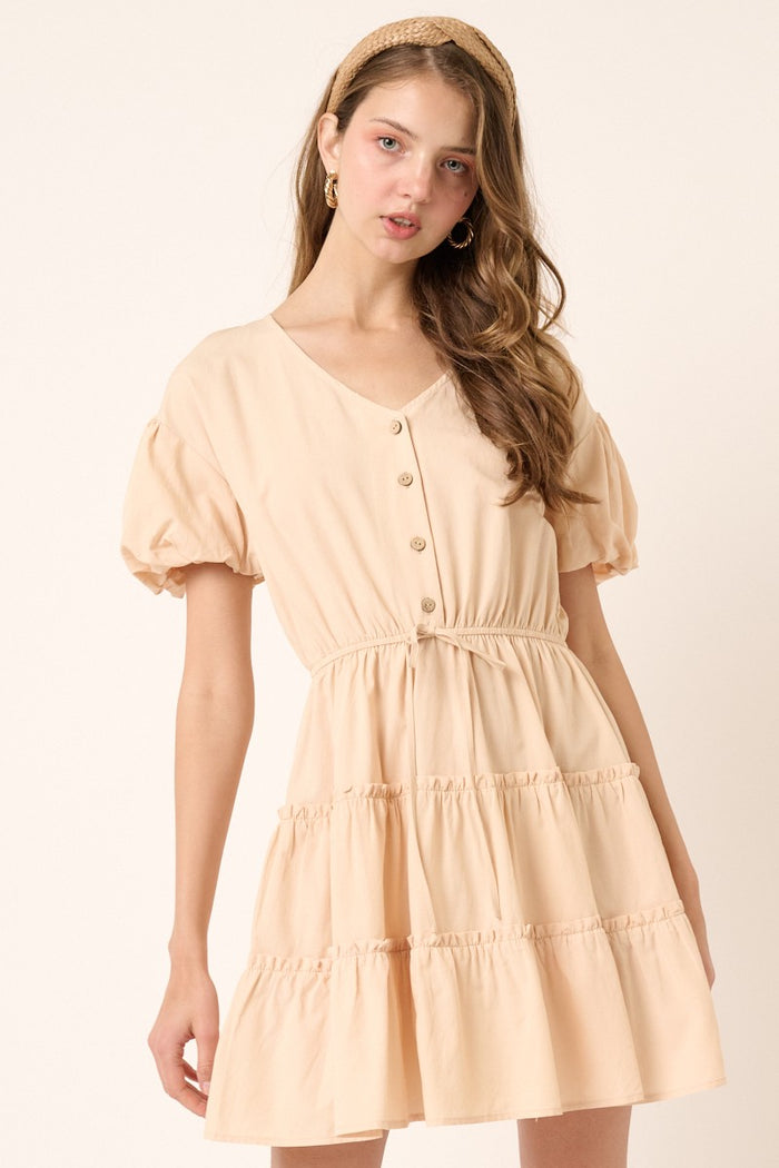 woman wearing a peach puff sleeve tiered dress with buttons and an elastic waist