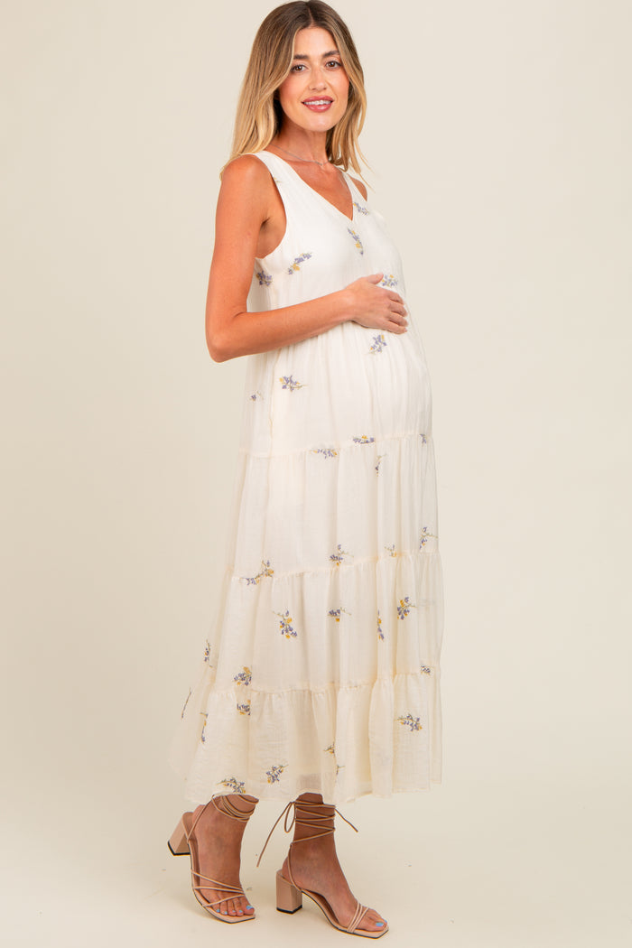 woman wearing a cream floral printed maternity maxi dress and holding her baby bump
