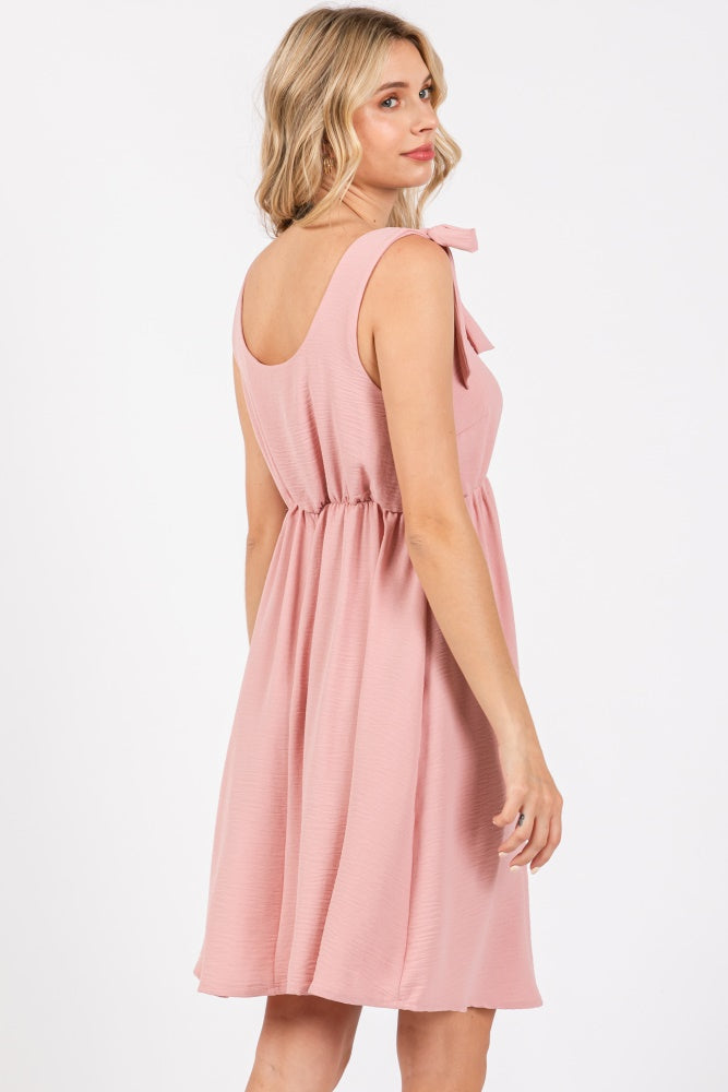 woman wearing a dusty pink sleeveless dress with a bow detail and an elastic waistband, shown from the back