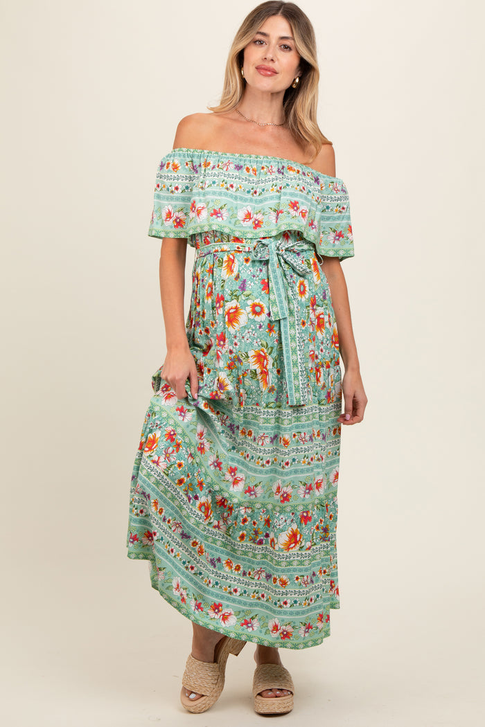 woman wearing a green off-the-shoulder floral maternity dress with a tie waist and a flowing maxi length