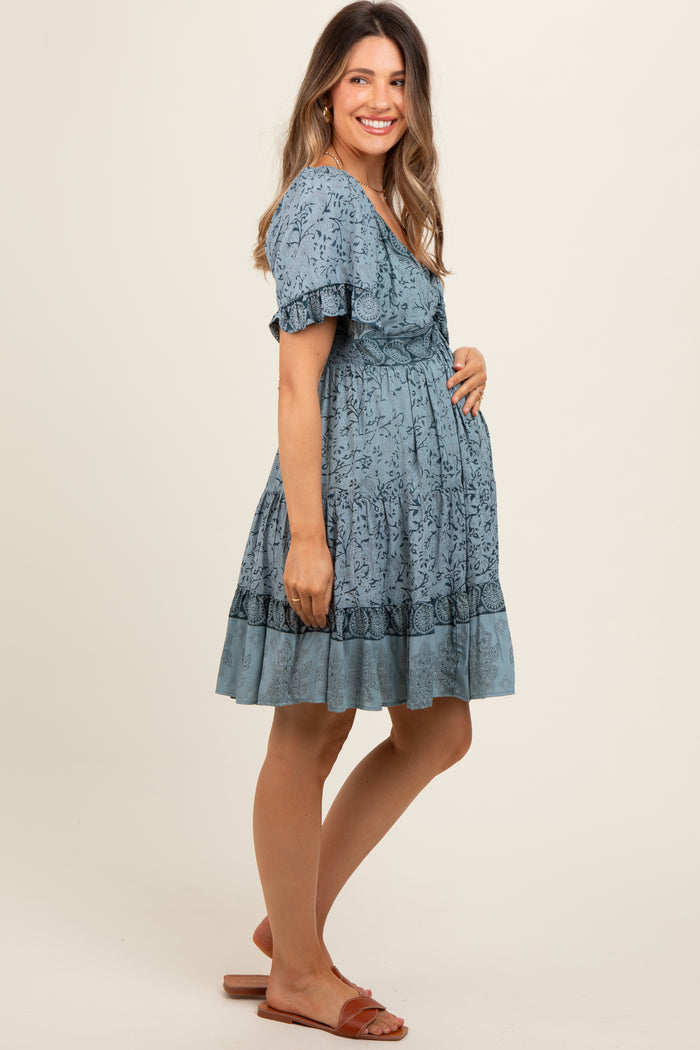 woman wearing a light blue floral maternity dress and holding her baby bump