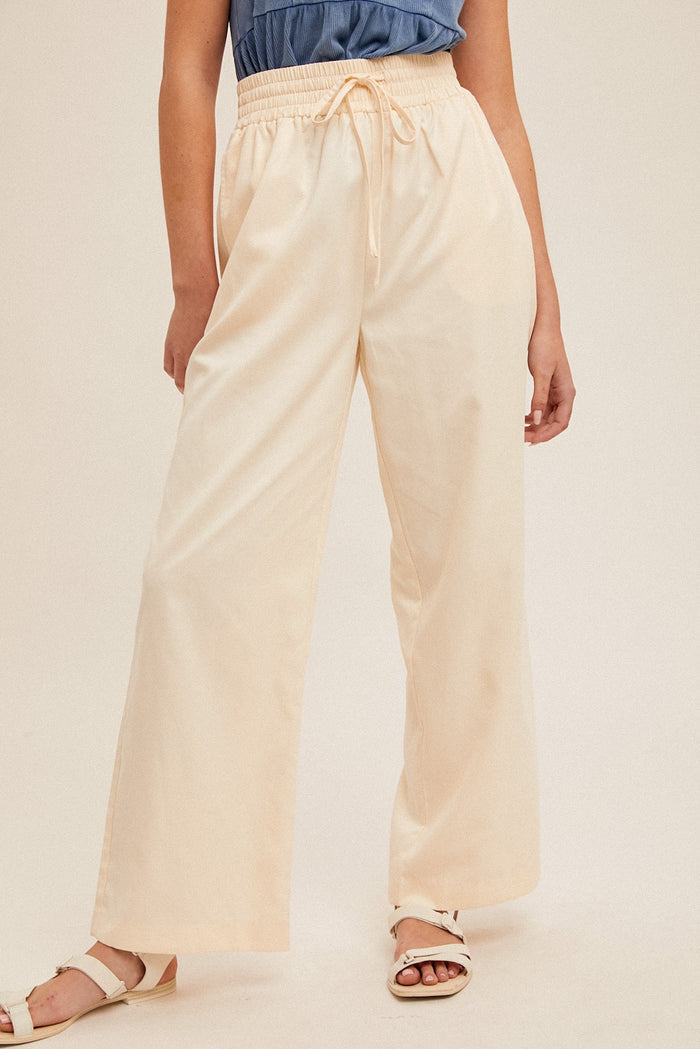 woman wearing cream wide-leg pants with an elastic waistband and drawstring, styled with a blue top