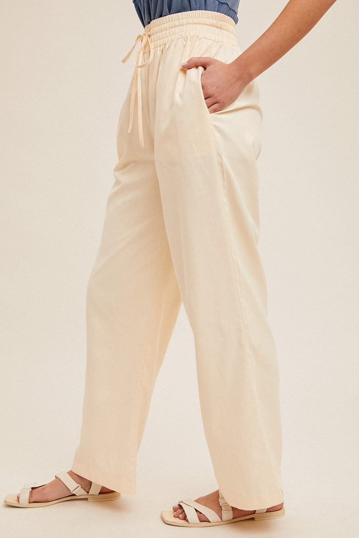 woman wearing cream wide-leg pants with elastic waistband and side pockets, paired with a denim top