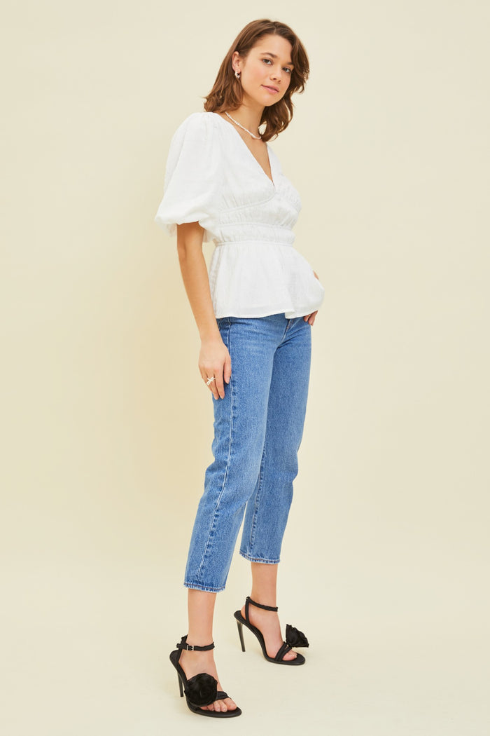 woman wearing a white puff sleeve peplum top paired with blue jeans and black high-heeled sandals