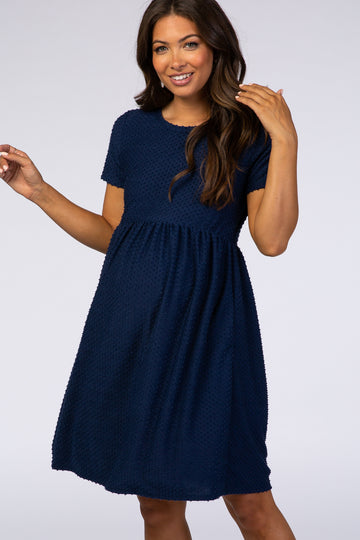 smiling woman wearing a navy blue short sleeve swiss dot maternity dress against a white background