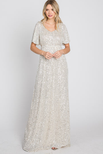 woman wearing a silver sequin maxi dress with flutter sleeves and a fitted waist