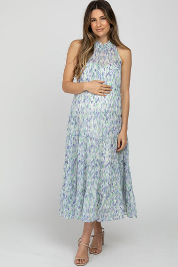 woman wearing a light green and purple floral maternity dress with a halter neck, gently holding her baby bump