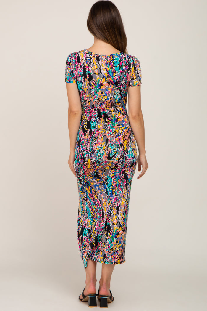 Back view of a woman wearing a colorful tropical print short sleeve maxi dress with black block heel sandals