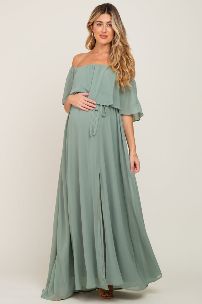 Pregnant woman wearing a sage green off-the-shoulder maternity maxi dress with a ruffled bodice and front slit