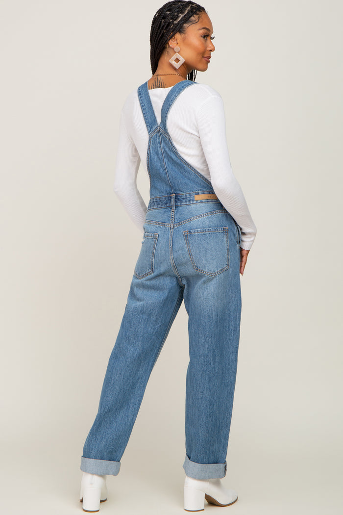 Woman wearing blue denim overalls and a white long sleeve shirt with white boots seen from the back