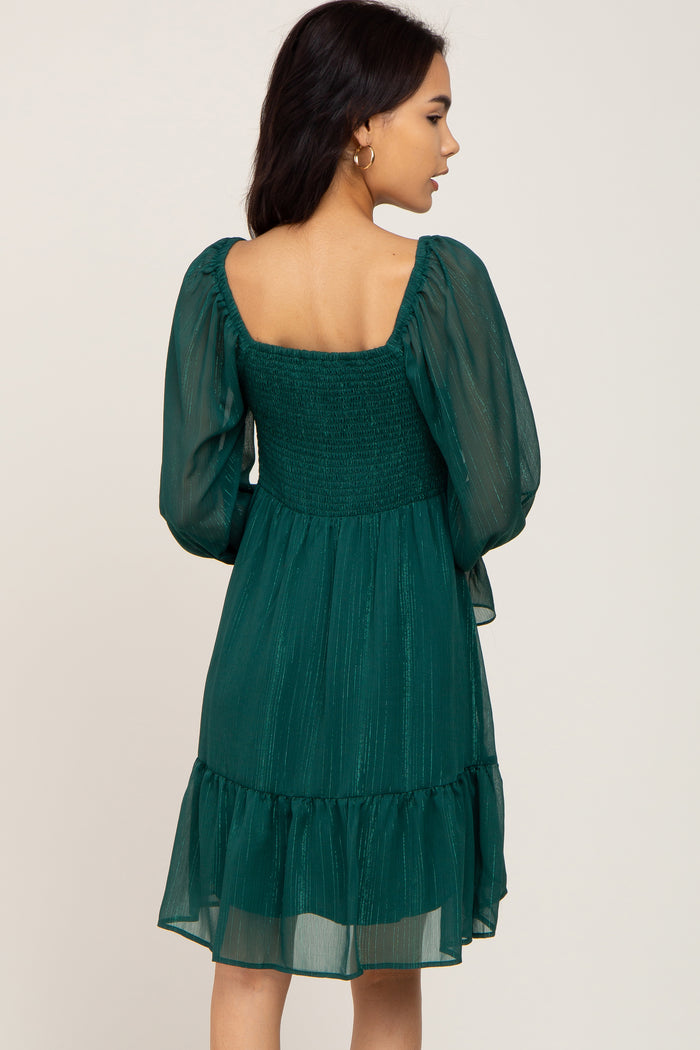 Back view of a woman wearing a dark green smocked mini dress with long sheer puff sleeves and metallic stripes