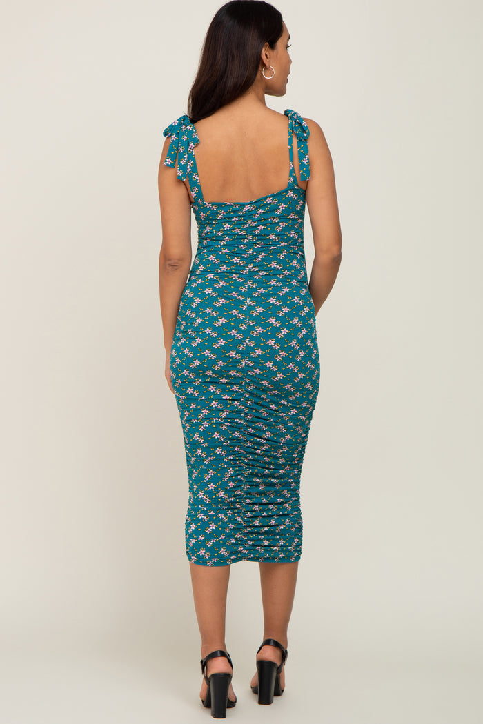 woman wearing a teal maternity dress with floral print and tie shoulder straps, showing a fitted silhouette