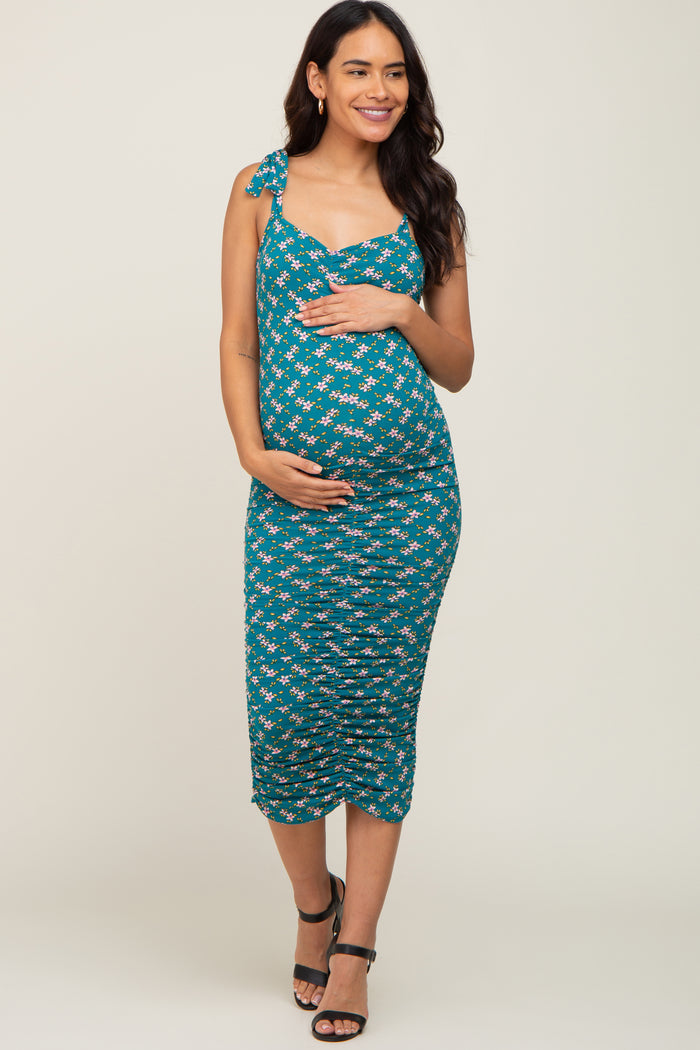 woman wearing a teal floral maternity dress with adjustable straps and a fitted silhouette, showing her baby bump