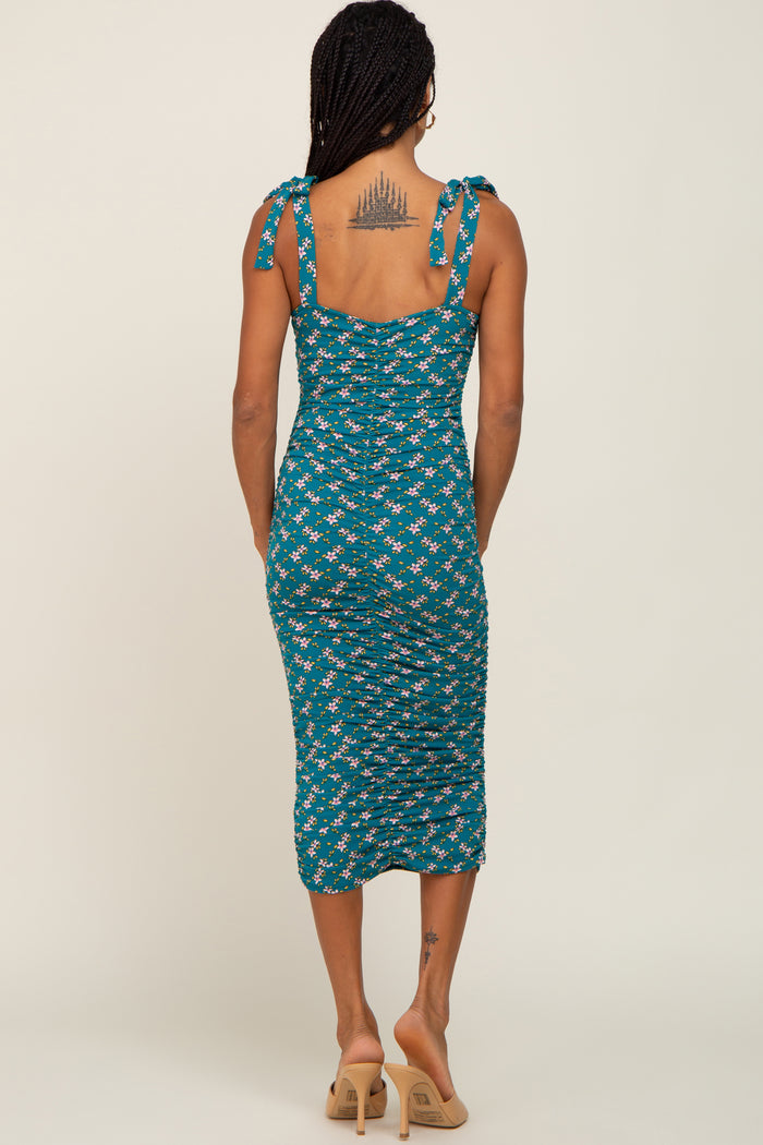 woman wearing a teal floral ruched midi dress with tie straps, showing the back and a tattoo on her upper back